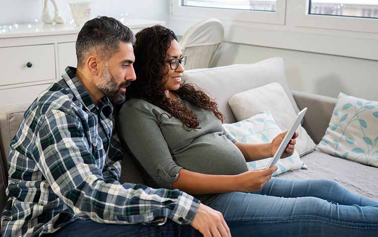 Pregnant woman with her partner on the sofa looking at a tablet