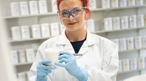 Woman in white coat with safety glasses holding white pot